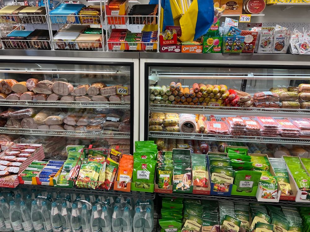 Deli case of cured meats and sausages beside shelves of imported seasonings, chocolate and pantry staples at Lviv International Food Store